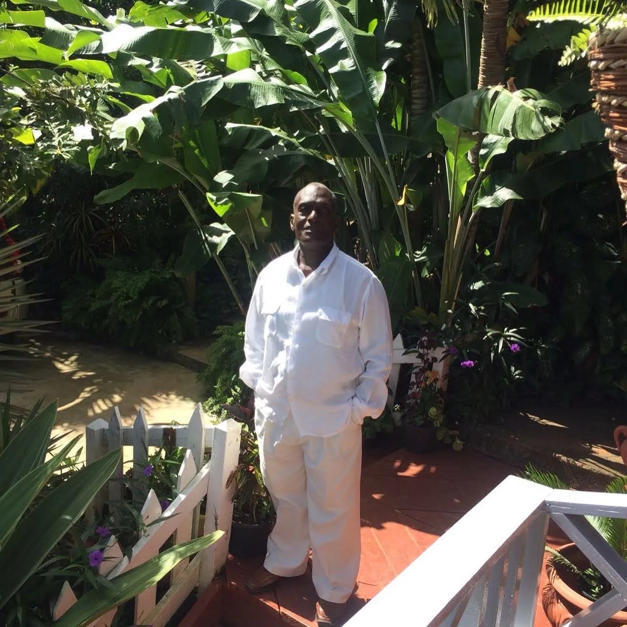 Lawrence Lambert in the garden, standing by the veranda among banana plants and flowers